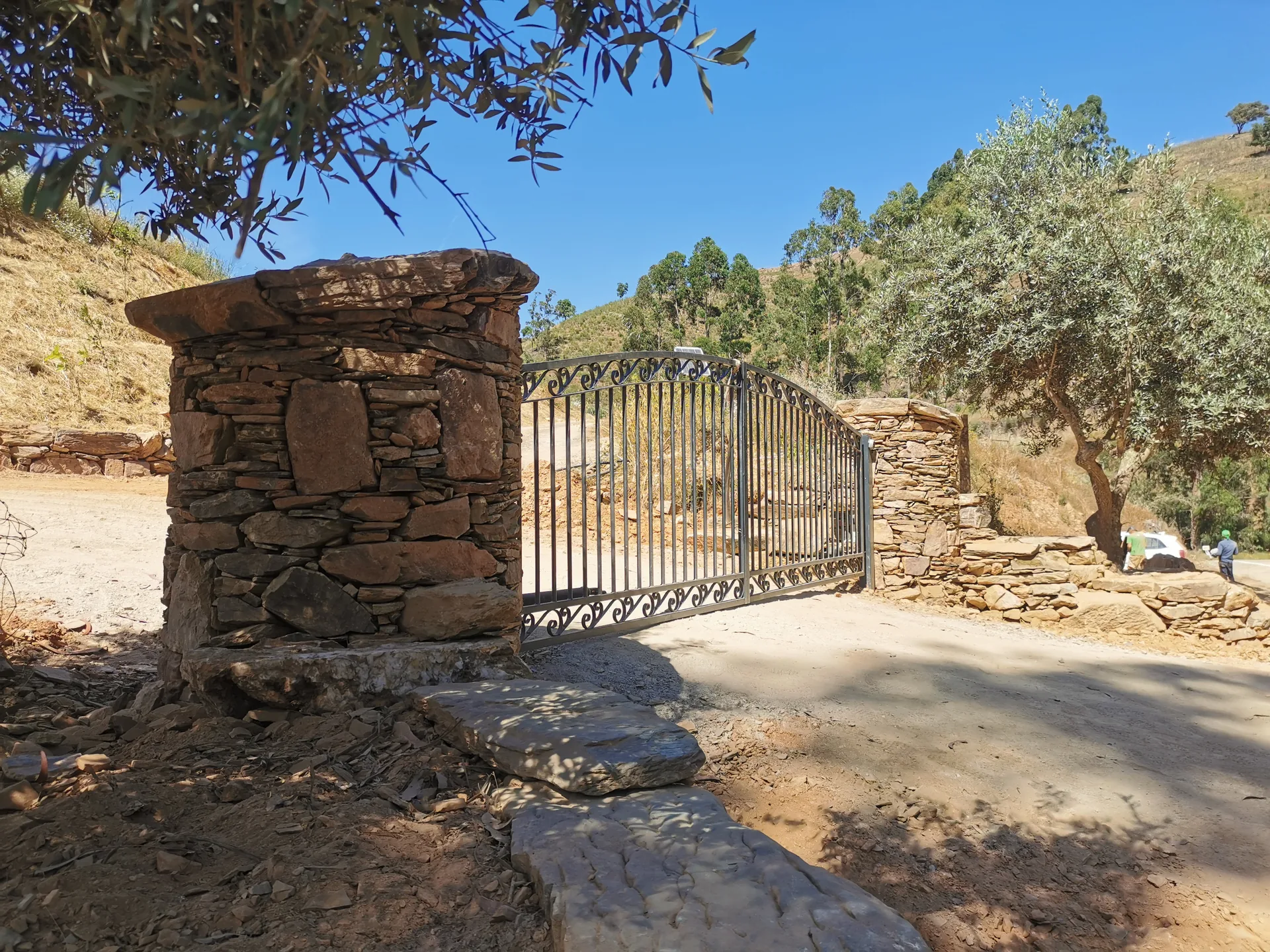 A dry stone gate pillar built of layered schist, framed by an olive tree, on a hillside track in the Alentejo