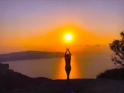 A figure with arms raised against the setting sun over the sea